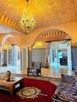 An ornate interior with a chandelier, patterned walls, and a red carpeted area.