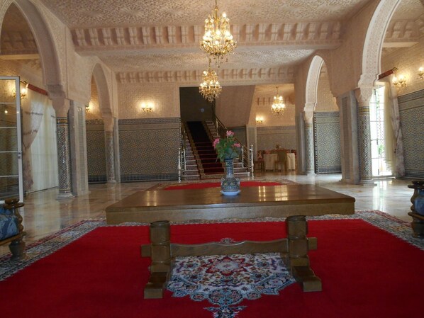 A grand lobby with a red carpet, ornate columns, a chandelier, and a staircase leading to upper floors. - Riad Dar Nador (Nador)