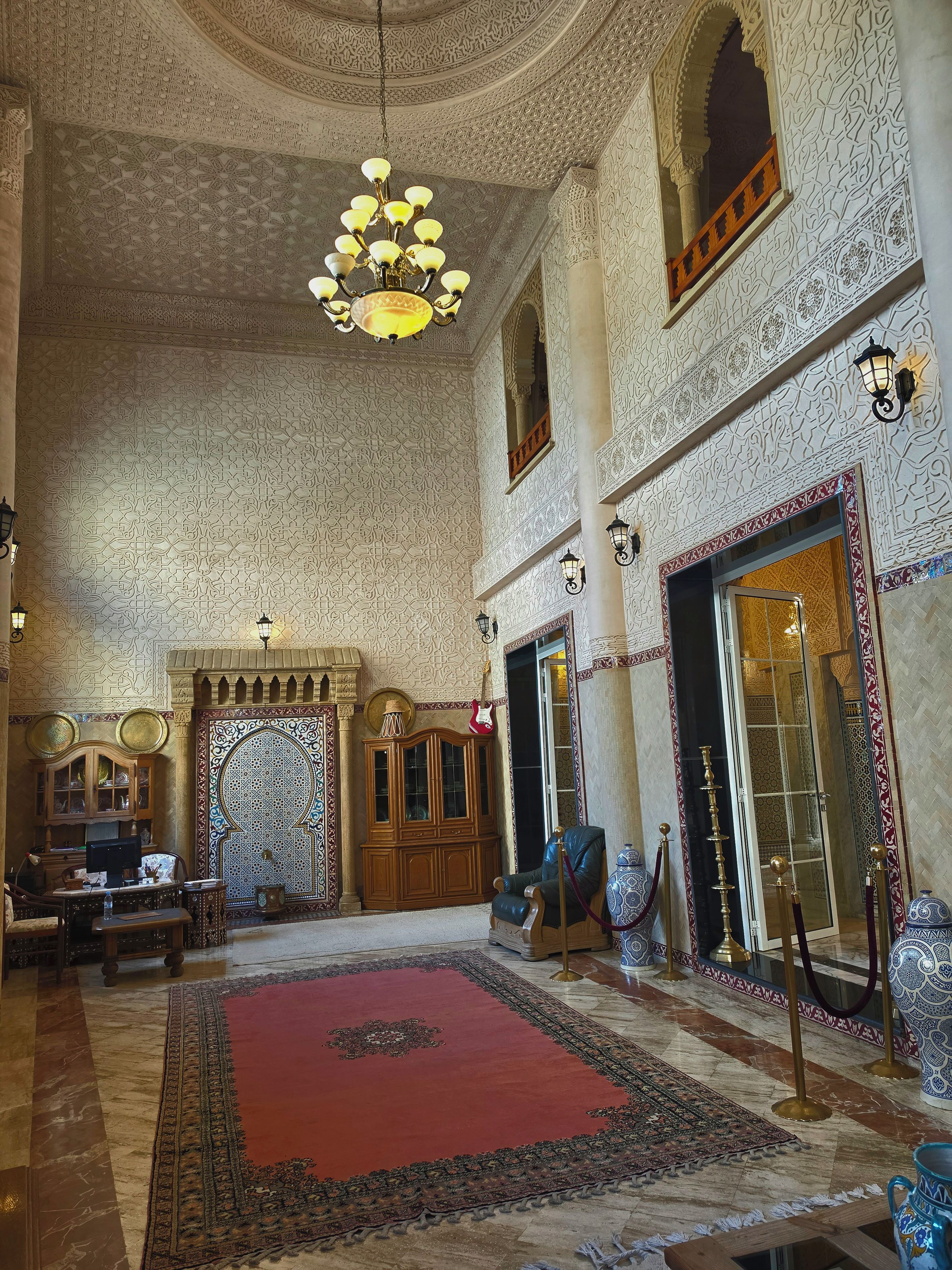 An ornate interior with a chandelier, a red carpet, and traditional furnishings.