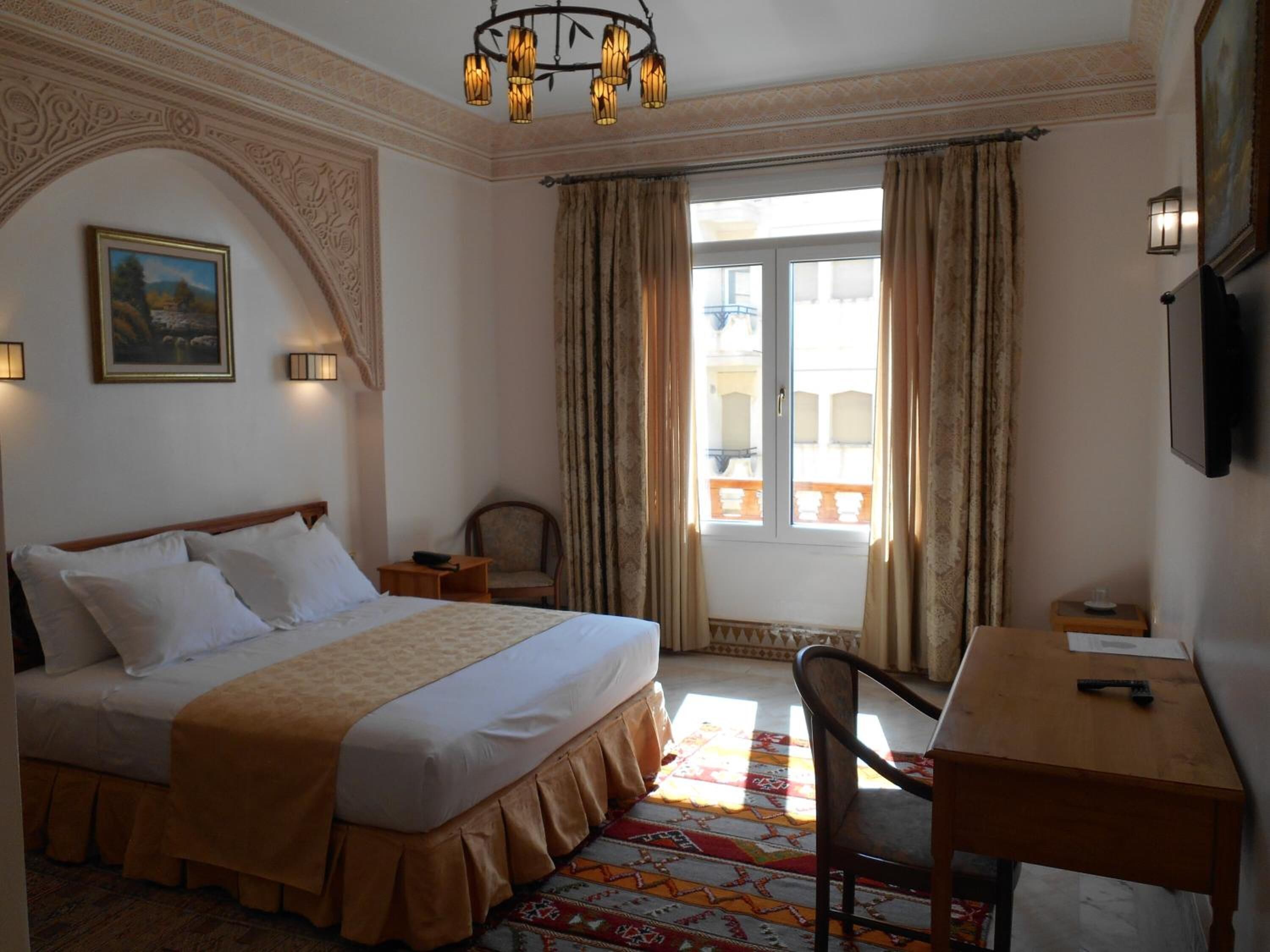 A hotel room with a large bed, a desk, a chair, a television, and a window with curtains.