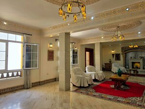 A spacious room with a red carpet, white chairs, a fireplace, and ornate ceiling decorations. - Riad Dar Nador (Nador)