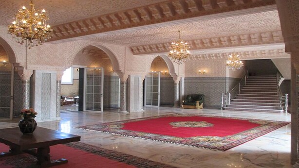 A spacious lobby with high ceilings, ornate chandeliers, and a large red carpet.