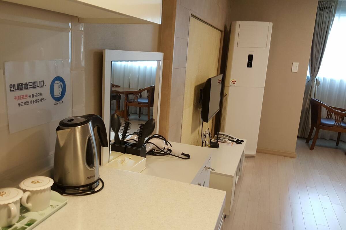 Habitación de hotel con kitchenette, cafetera, secador de pelo y espejo que refleja un comedor.