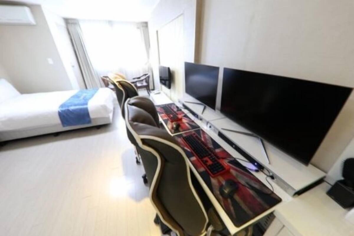 Habitación de hotel compacta con una cama, un escritorio con dos monitores y una silla.