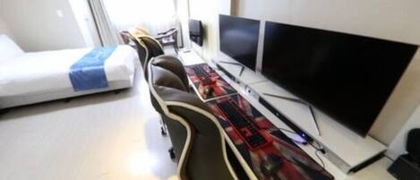 Une chambre d’hôtel de taille réduite, comprenant un lit, un bureau avec deux écrans et une chaise.