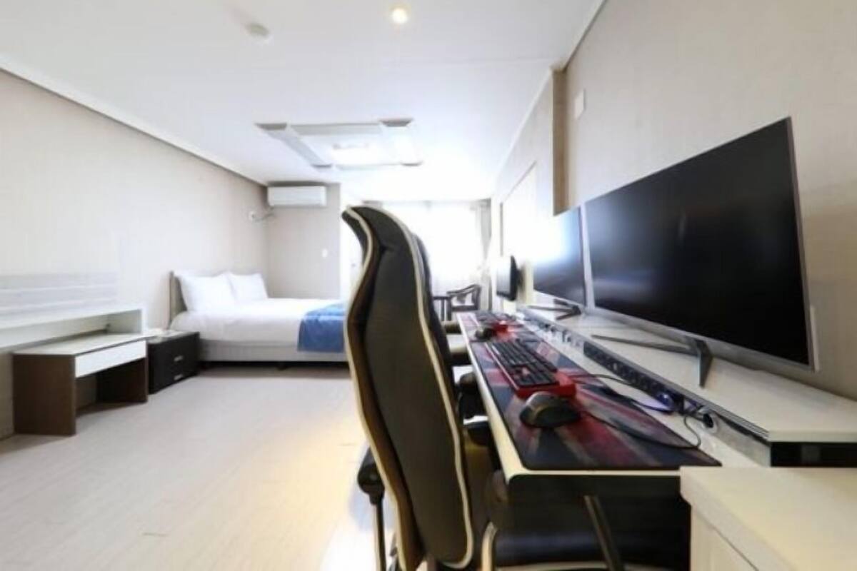 Una habitación de hotel moderna con una cama, un escritorio con ordenador, un televisor grande y una silla.