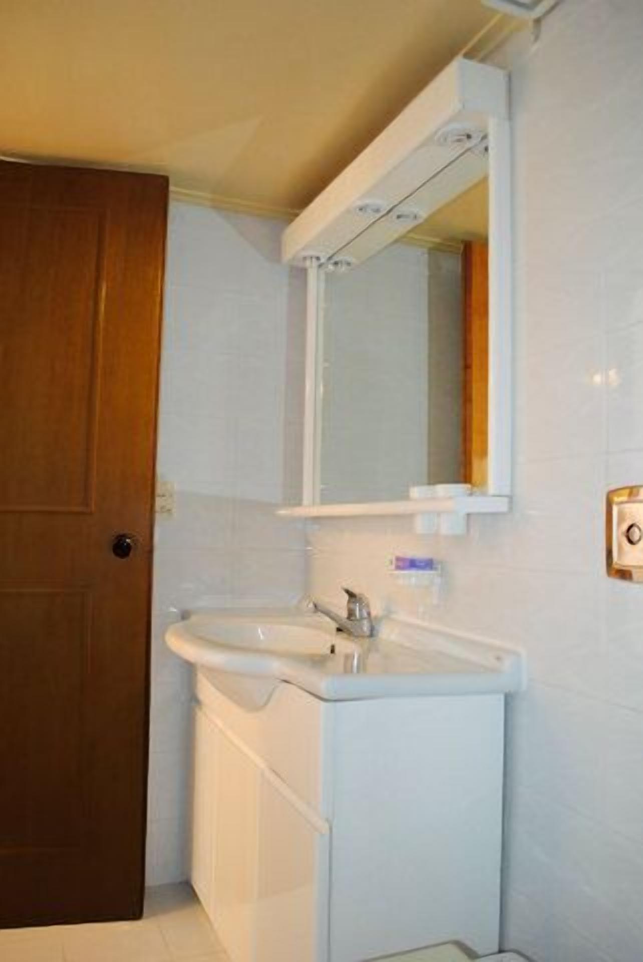 Un baño con puerta de madera, un lavamanos blanco y un espejo encima.