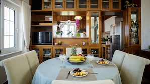A dining area with a round table, chairs, a television, and a kitchen in the background. - Star Daratsos (Chania)