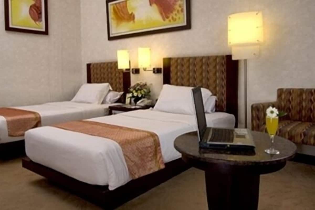 Ein Hotelzimmer mit zwei Einzelbetten, einem kleinen runden Tisch mit einem Laptop und einem Glas Saft sowie einer Couch.