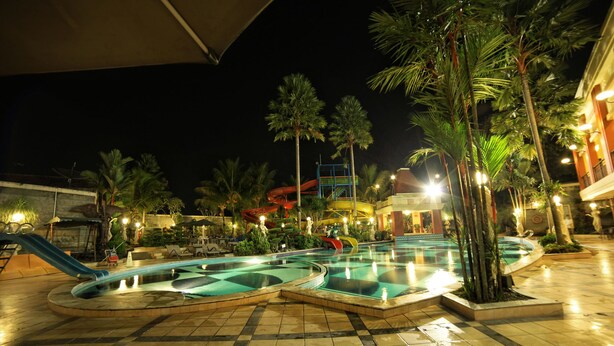 A nighttime swimming pool area with multiple pools, palm trees, and a water slide. - Grand Wahid Hotel Salatiga (Salatiga)