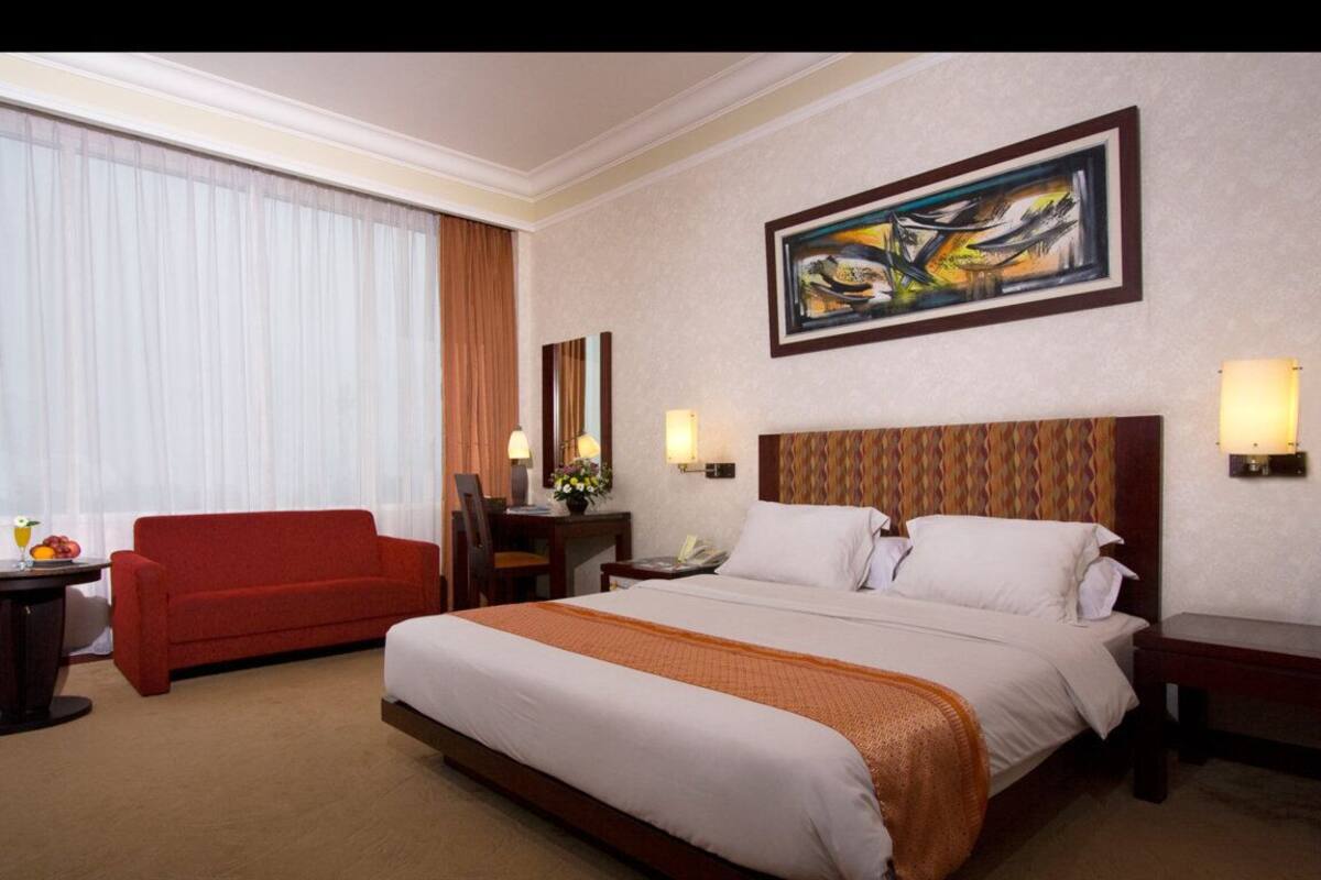 Ein Hotelzimmer mit einem großen Bett, einem roten Sofa, einem Schreibtisch mit Lampe sowie einem Bild an der Wand.