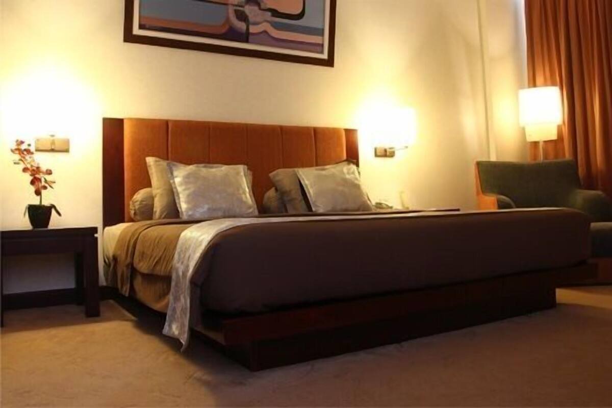 Ein Hotelzimmer mit einem großen Bett, zwei Nachttischlampen, einem grünen Sessel und einem Bild an der Wand.