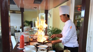 A chef cooking with flames on a stove in a restaurant setting. - Grand Wahid Hotel Salatiga (Salatiga)