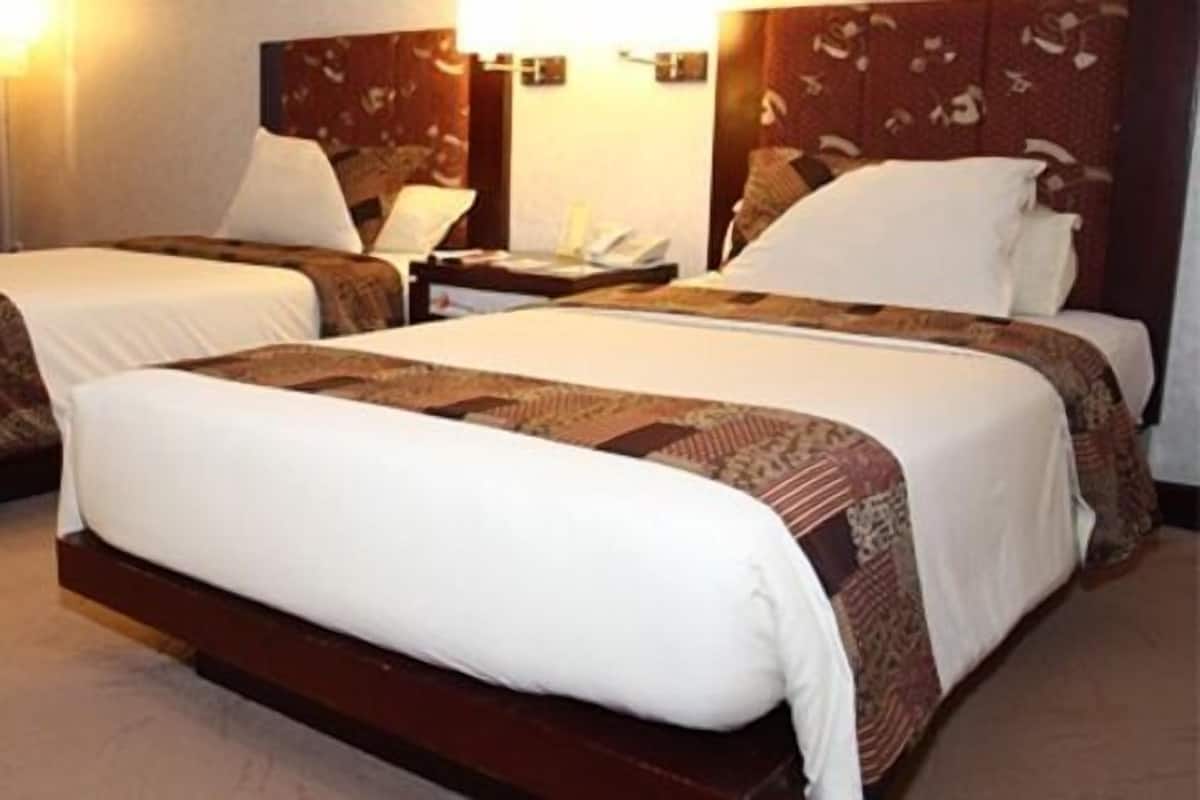 Ein Hotelzimmer mit zwei Einzelbetten, jeweils mit Holz Kopfteil und weißer Bettwäsche. An einer Seite befindet sich ein Nachttisch mit Lampe und Telefon.