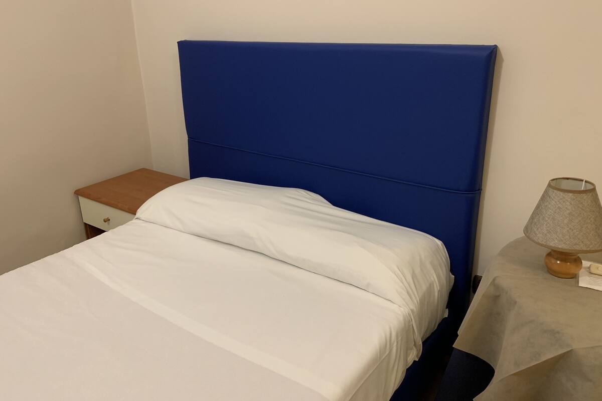 A bed with a blue headboard, a bedside table with a lamp, and a small drawer.