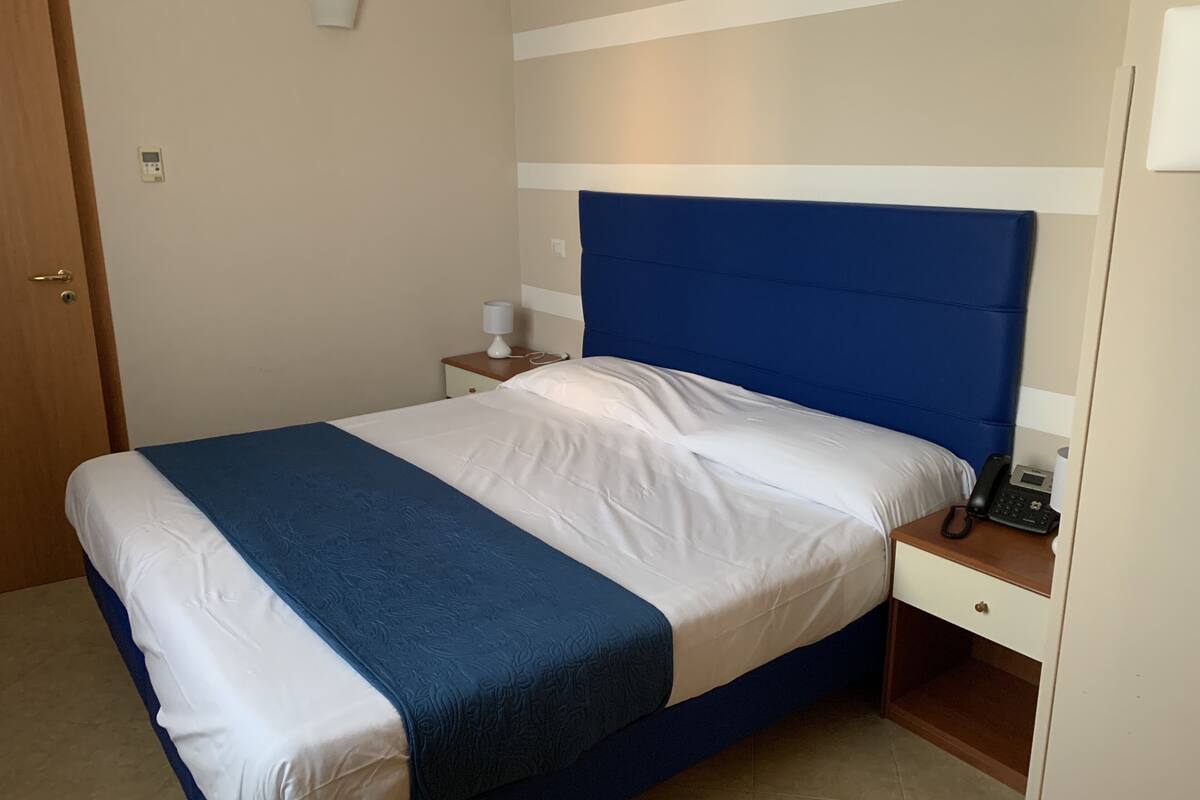 A neatly made bed with a blue headboard, a bedside table with a lamp, and a phone on the nightstand.