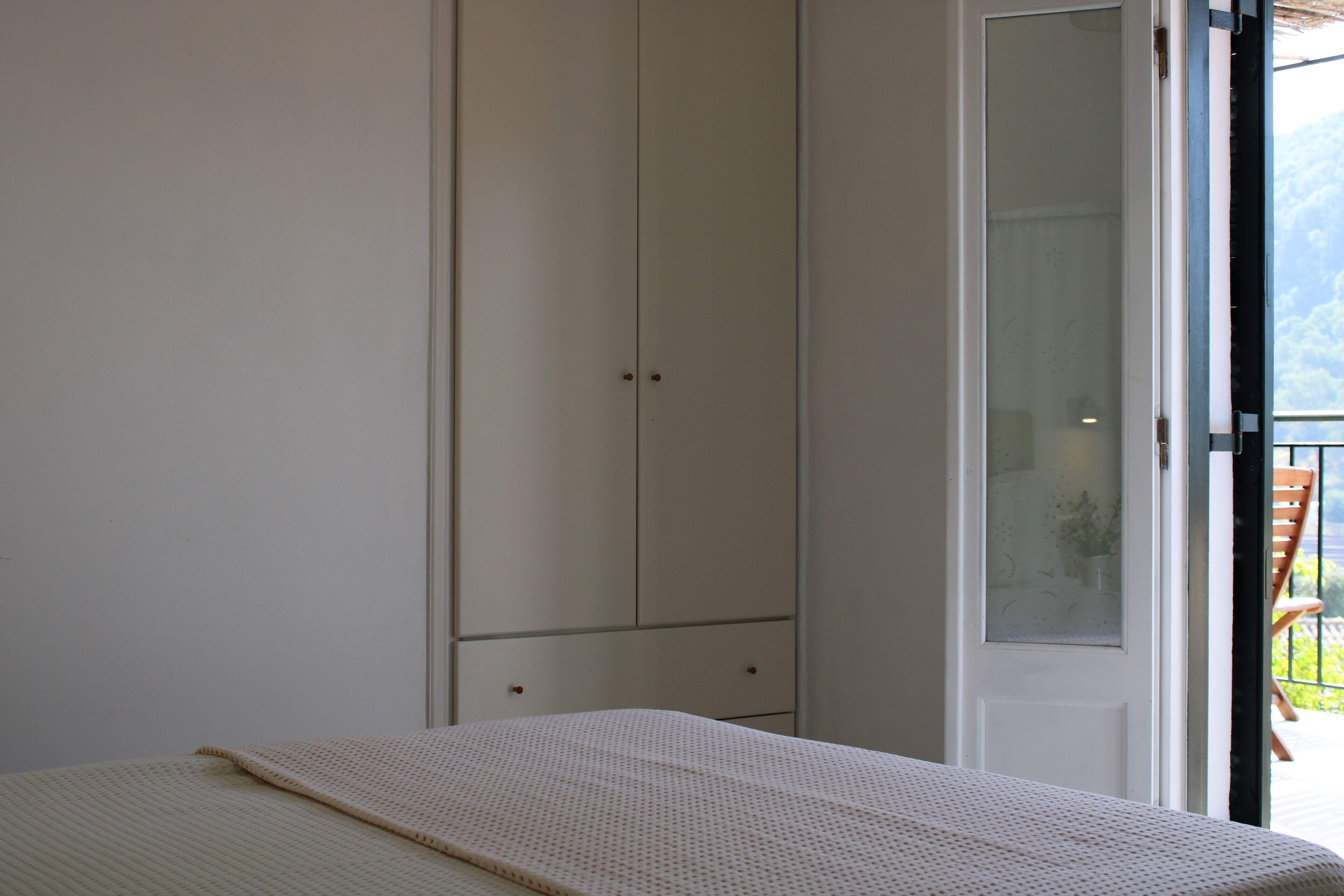 A bedroom with a bed, a wardrobe, and a door leading to an outdoor balcony.