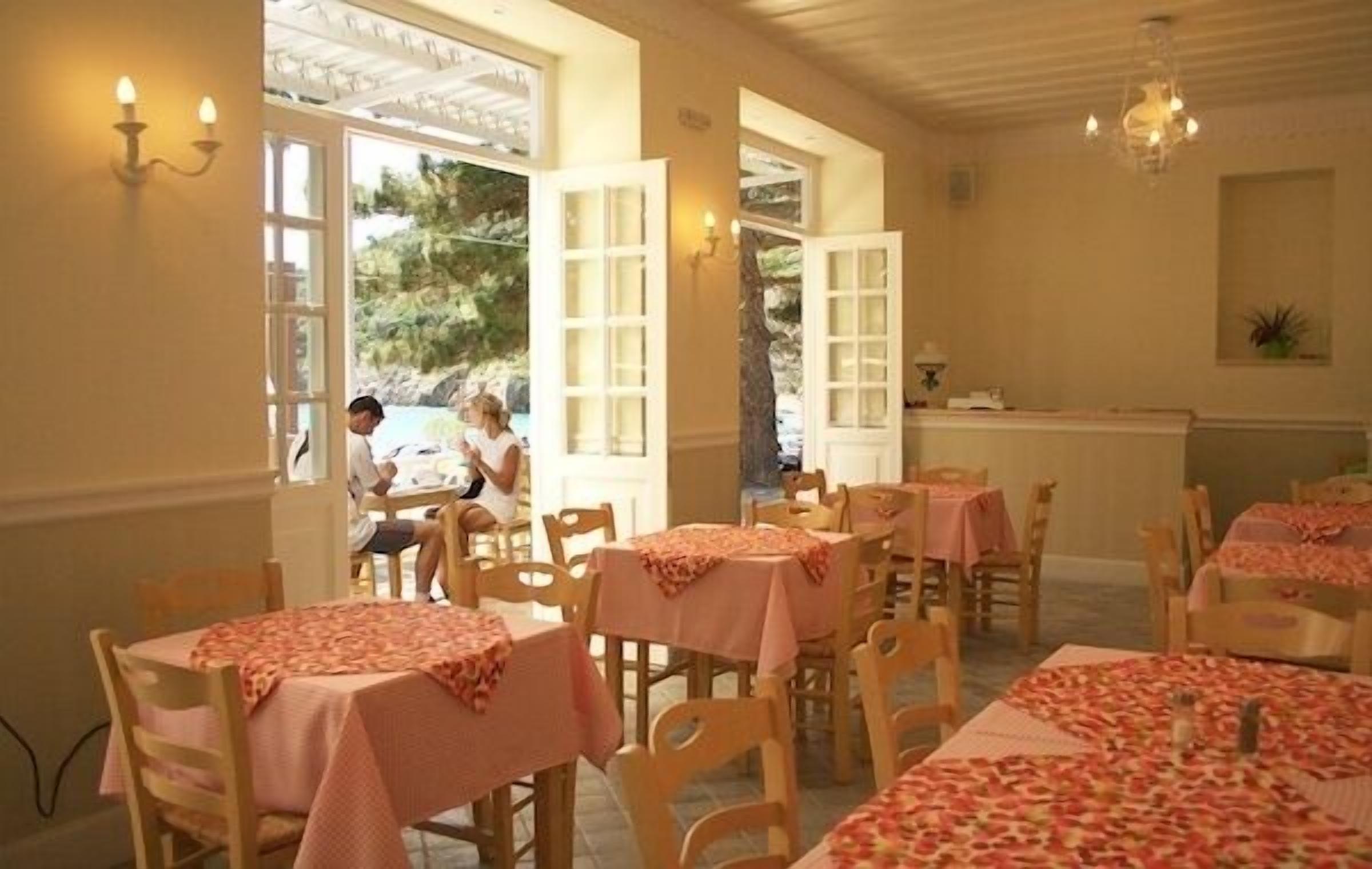 A restaurant with tables covered in pink tablecloths, wooden chairs, and open windows with white frames.