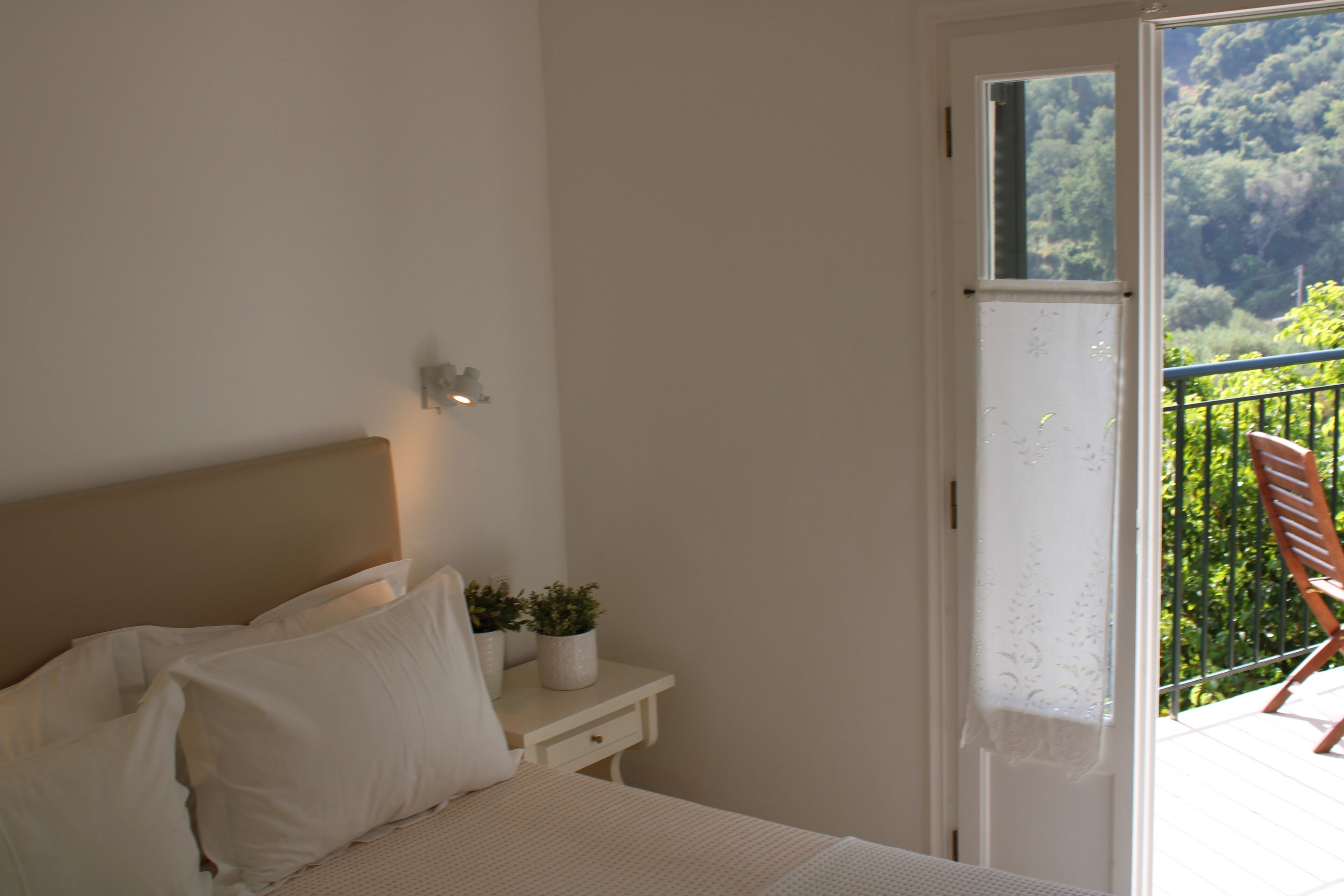A bedroom with a bed, bedside table, and a view of a balcony with a chair.
