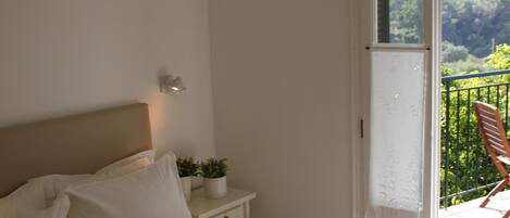 A bedroom with a bed, bedside table, and a view of a balcony with a chair.