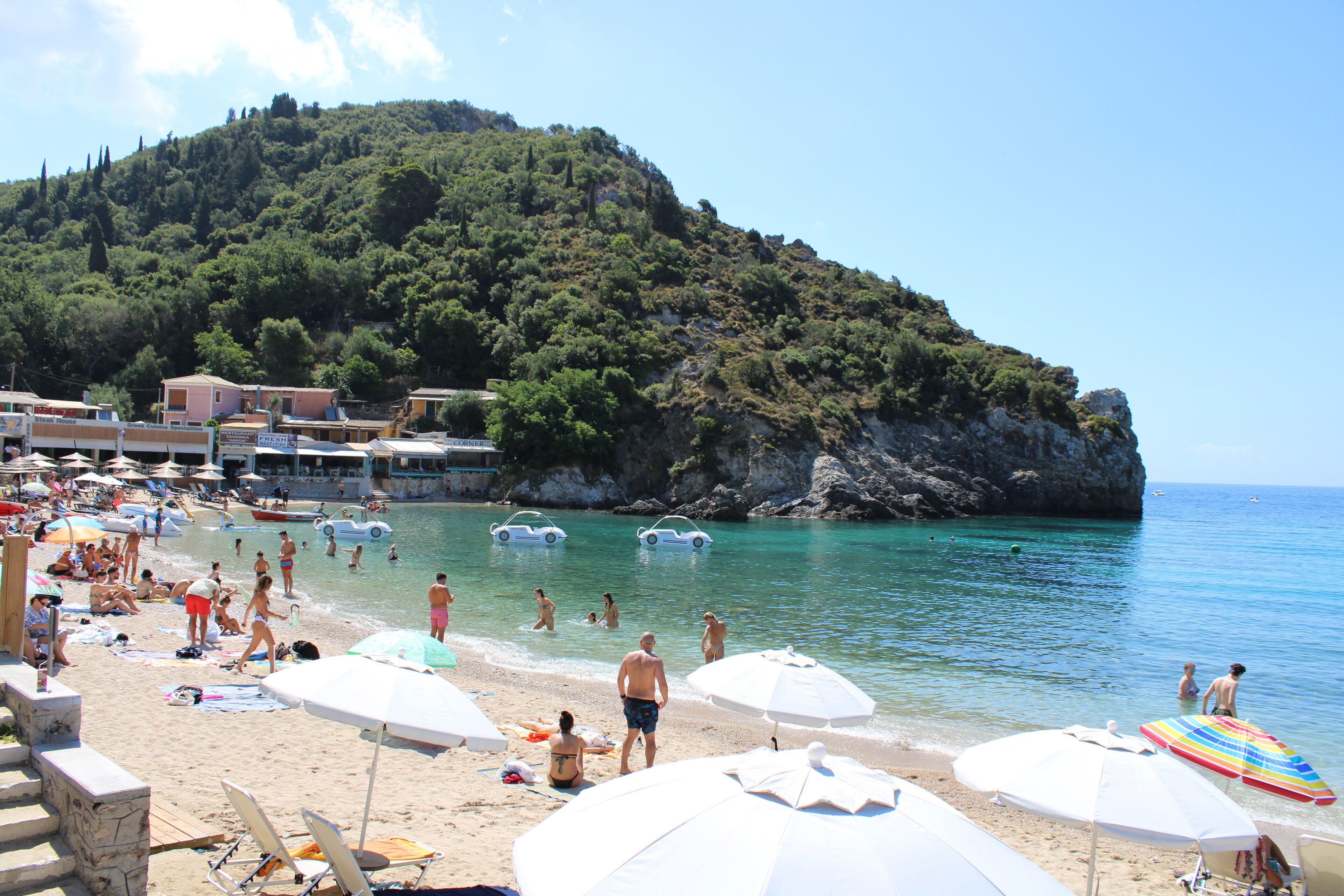 Una playa con sombrillas, gente y barcos.