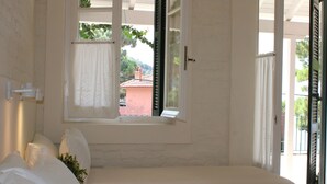 A bedroom with a bed, a window with curtains, and a view of a building outside. - Zefiros Traditional Hotel (Corfu)