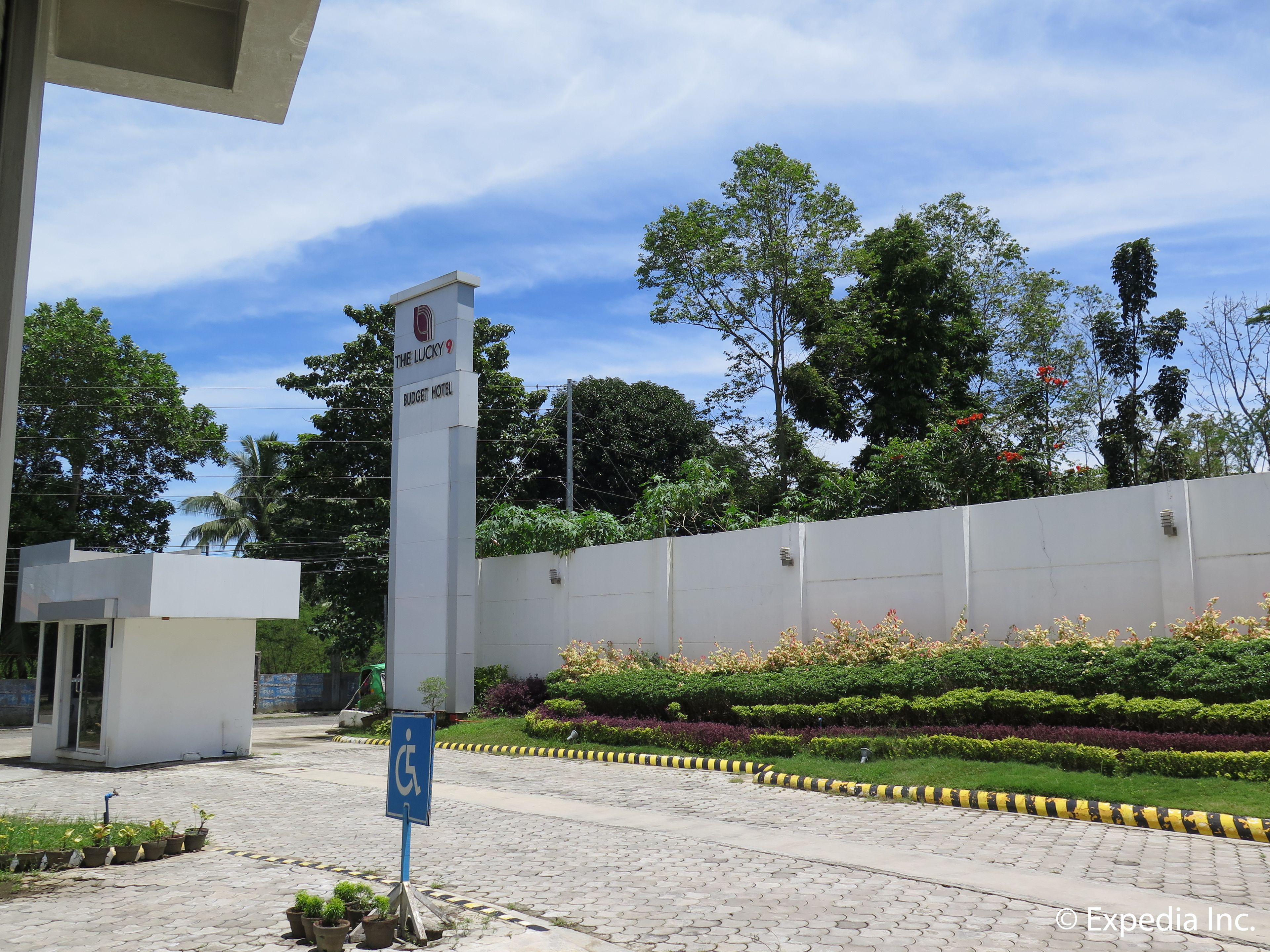 A sign for The Lucky 9 Budget Hotel, surrounded by a landscaped garden with a paved walkway and a wheelchair accessibility sign.