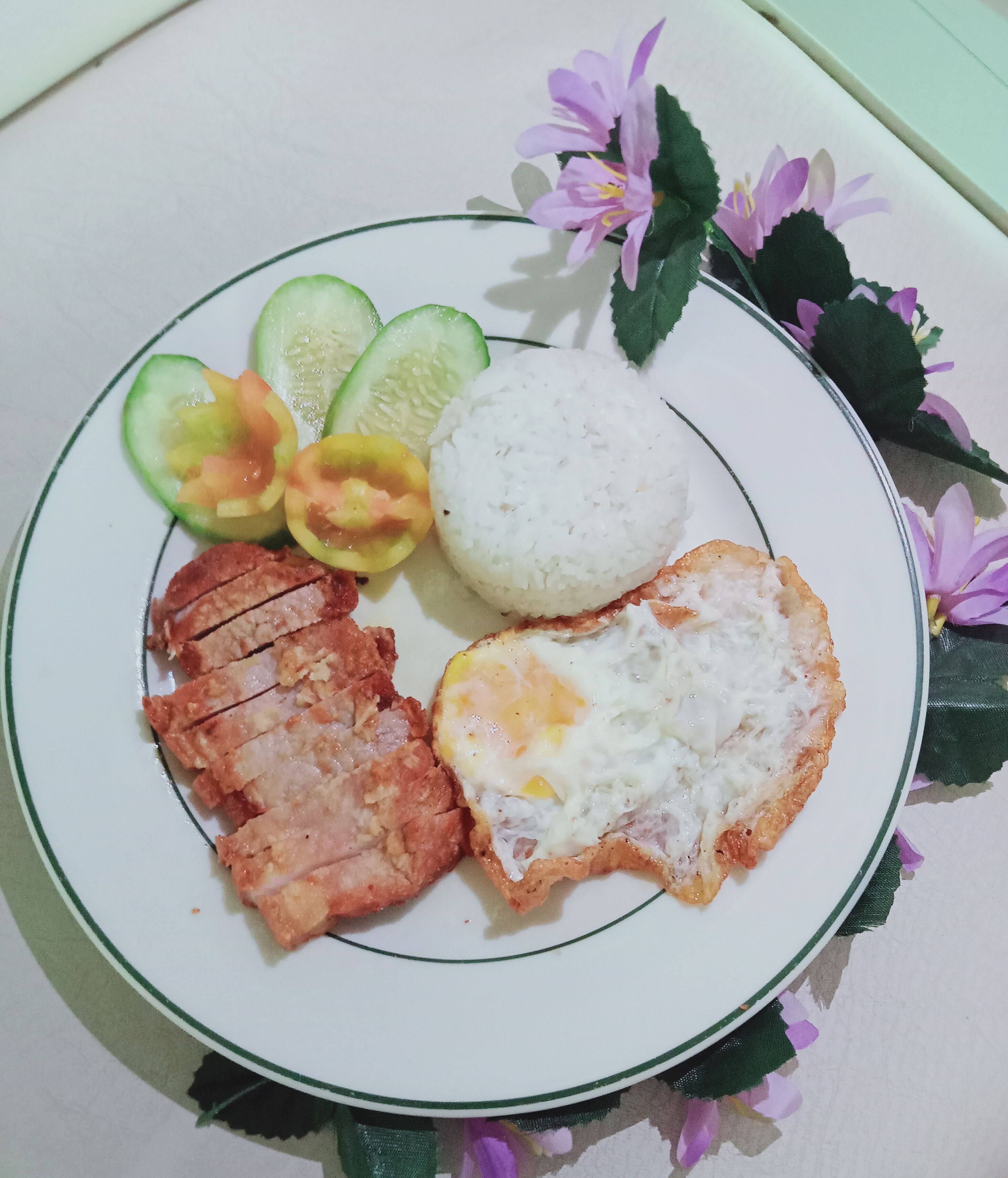 A plate with sliced meat, a fried egg, rice, and sliced vegetables.