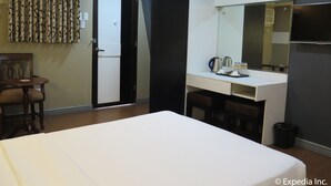 Ein Hotelzimmer mit Bett, Schreibtisch mit Spiegel, Stuhl, kleinen Tisch und Mülleimer.