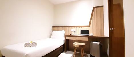 A hotel room with a single bed, a desk with a laptop, a small stool, and a suitcase.