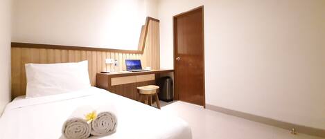 A hotel room with a bed, a desk, a laptop, and an air conditioner.