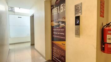 A hotel corridor with a lift, fire extinguisher, and a poster advertising a meeting package.