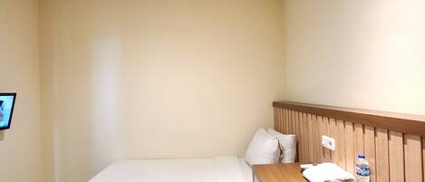 A small, neatly arranged hotel room with a single bed, a wooden desk, and a chair.