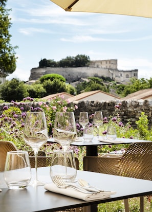 An outdoor dining table with wine glasses and cutlery, set against a backdrop of a historic building and lush greenery. - La Ferme Chapouton - Teritoria (Grignan)