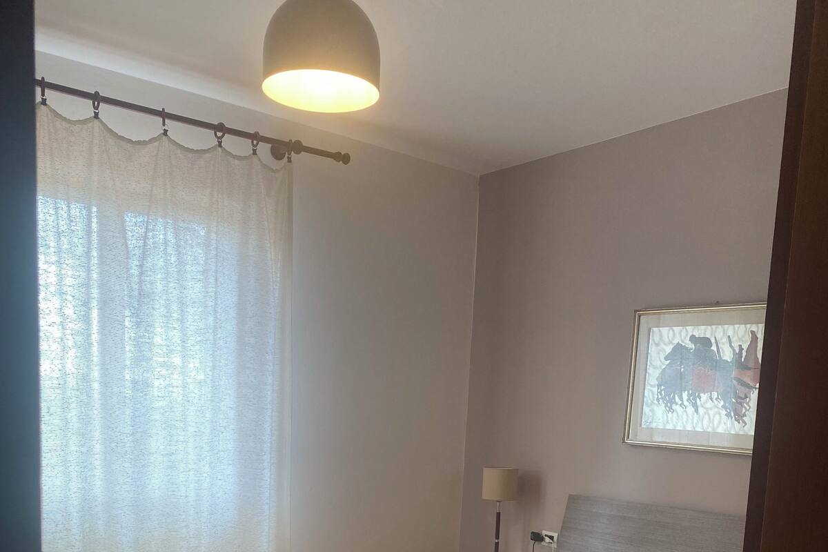 A bedroom with a large bed, wooden flooring, a ceiling light, a nightstand, and a wall-mounted lamp.