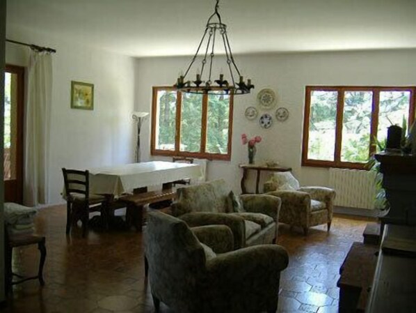 A room with a dining table, chairs, a chandelier, and large windows.