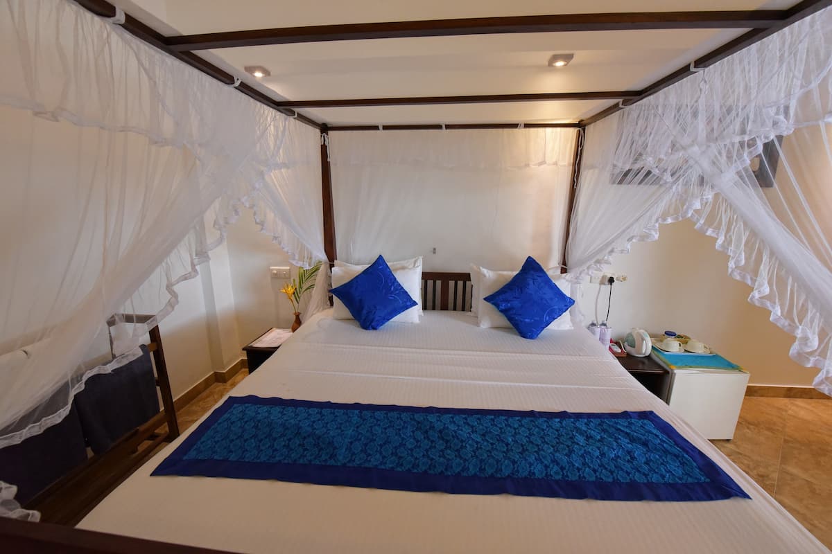 A bedroom with a large bed, white canopy, blue pillows, and a blue bed runner.