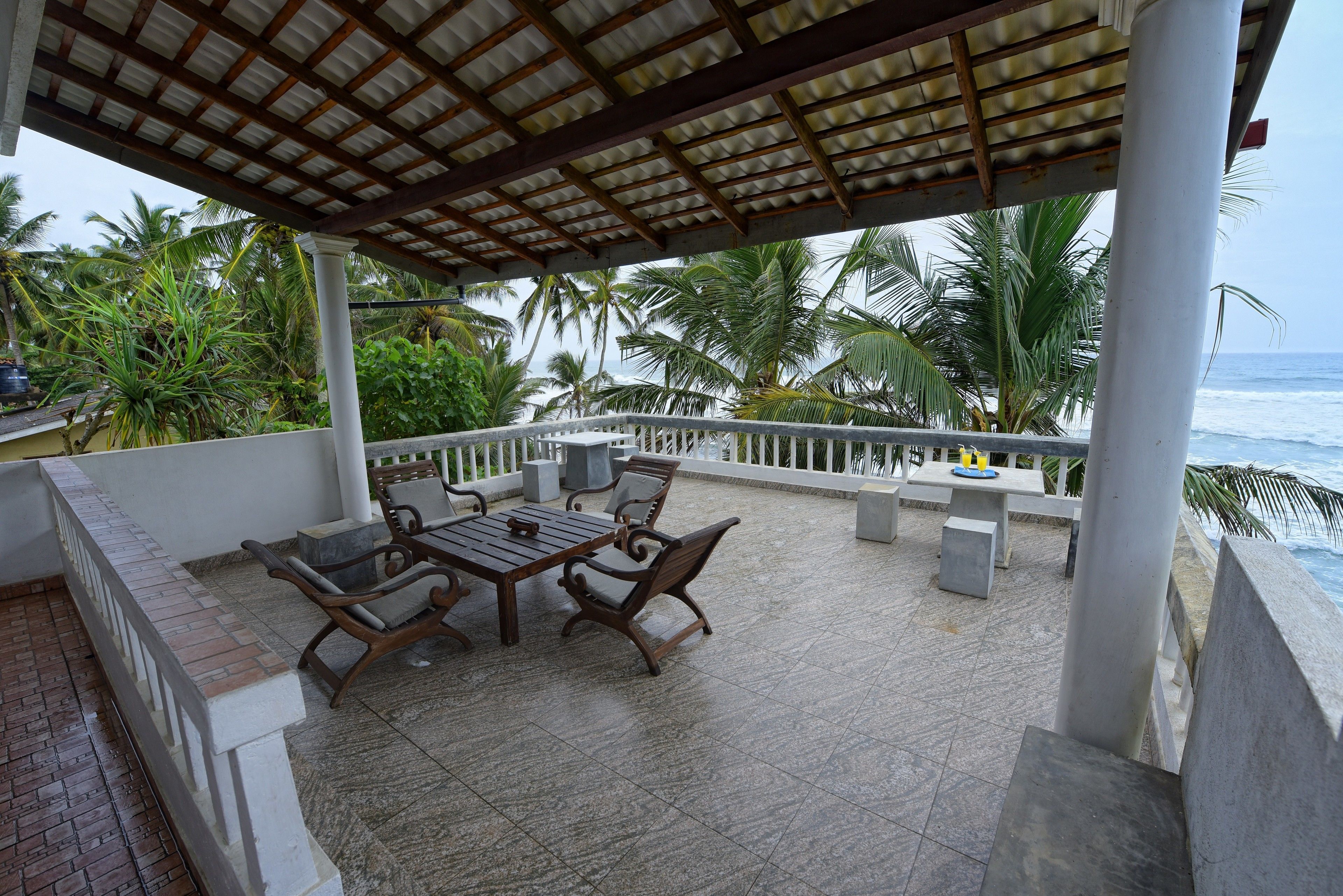 A covered outdoor seating area with a table and chairs, overlooking the ocean.