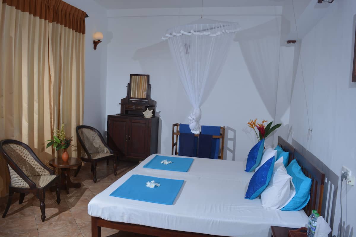 A neatly arranged bedroom with a bed, two blue placemats, a bedside table, a chair, a small table with a vase, and a nightstand.