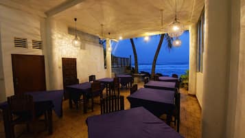An indoor dining area with tables and chairs, a wooden door, and a view of the ocean at dusk.