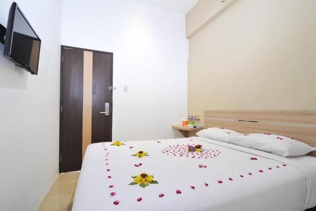 A hotel room with a bed, a TV mounted on the wall, and a wooden door.