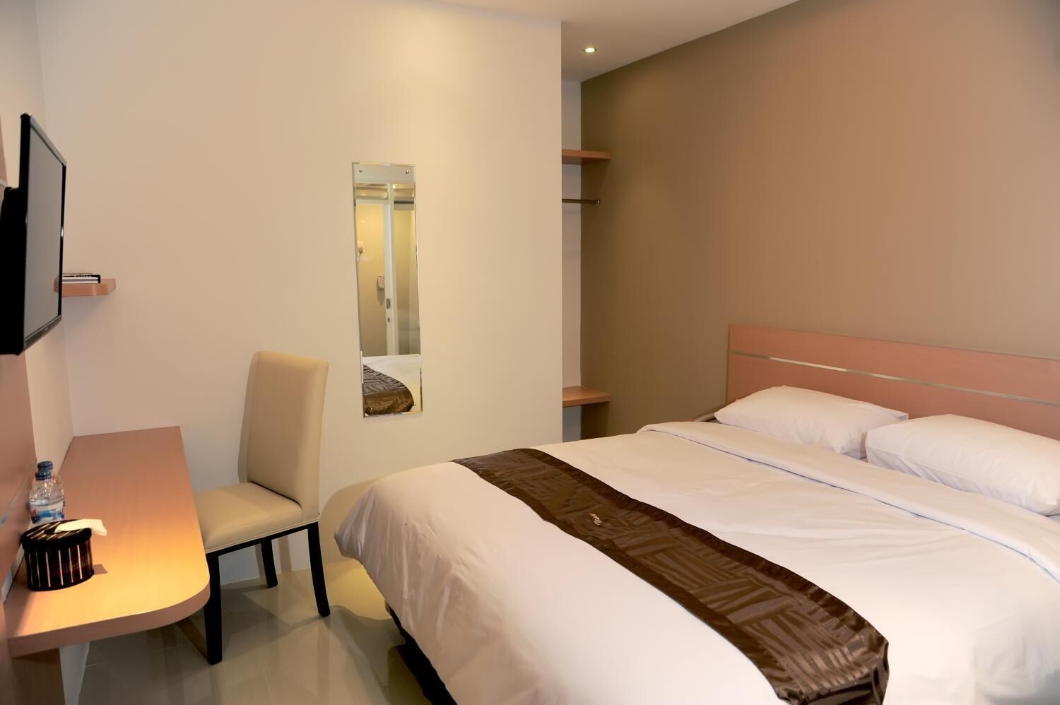 A hotel room with a bed, a chair, a desk, a television, and a mirror.
