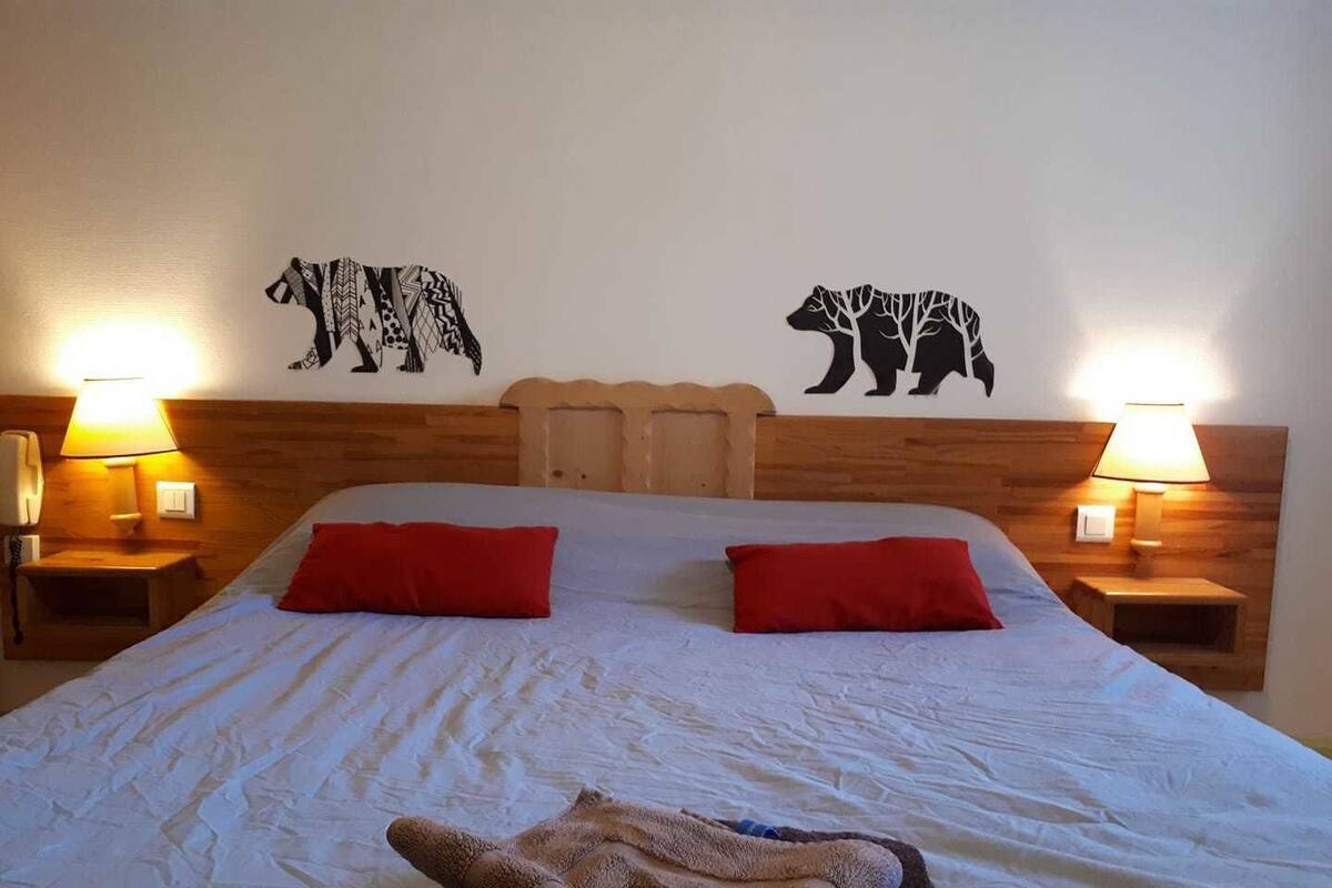Hotellihuone, jossa on puinen pääty, kaksi punaista tyynyä, peitto ja seinätaideteos, jossa on kuvattuna karhuja.