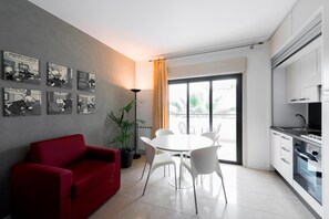 A modern living room with a red sofa, a dining table with chairs, a potted plant, and a large window with curtains. - Residence Annunziata (Messina)