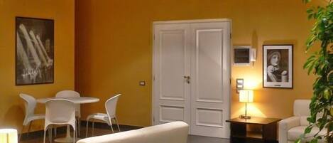 A hotel room with a red ceiling, yellow walls, a white sofa, a dining table with chairs, a small desk, and a lamp.