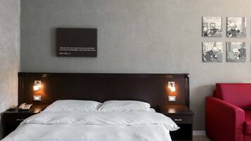 Een hotelkamer met een groot bed, nachtkastjes met lampen, een rode stoel en kunst aan de muur.