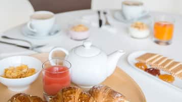 A breakfast table with croissants, a teapot, coffee cups, and a glass of orange juice.