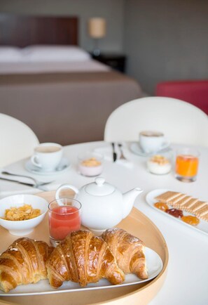 A breakfast table with croissants, a teapot, coffee cups, and a glass of orange juice. - Residence Annunziata (Messina)