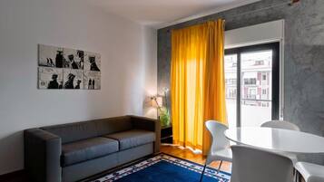 A modern living room with a grey sofa, a blue rug, a white table, and yellow curtains.