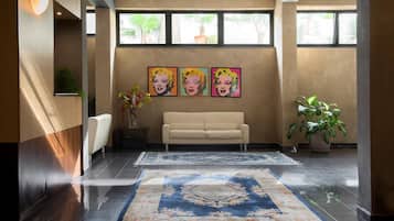 A modern lobby with a beige sofa, two large rugs, and three pop art style paintings on the wall.